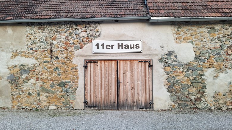 Au&szlig;enansicht des 11er Hauses mit Holztor und Steinmauer.