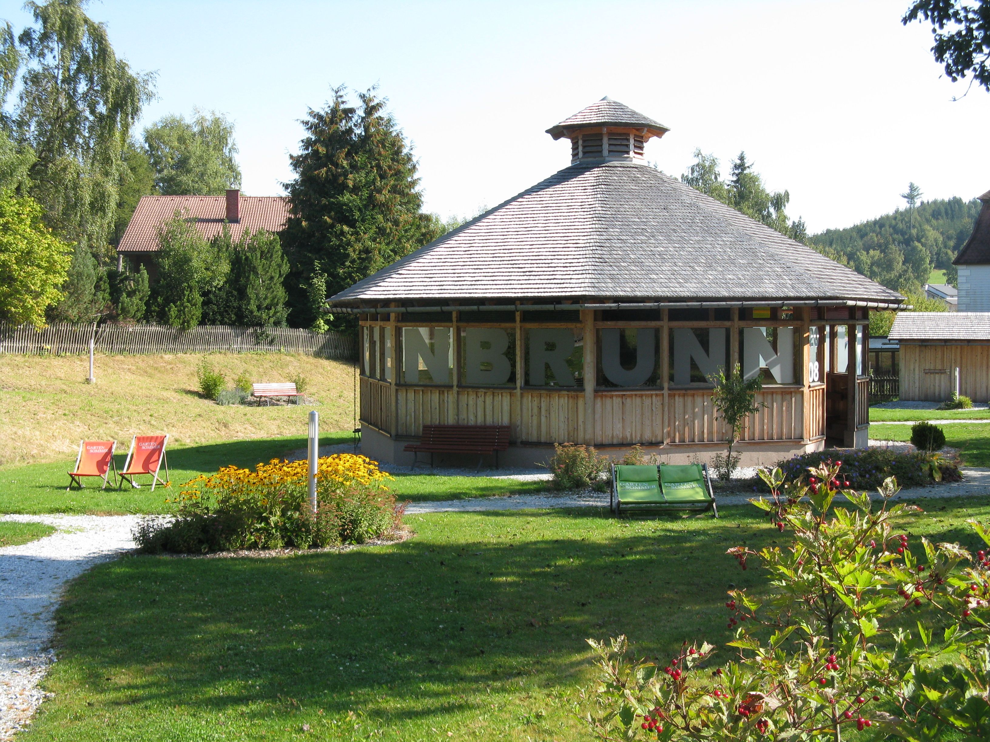 Pavillon in einem grünen Park mit Blumen und Liegestühlen.