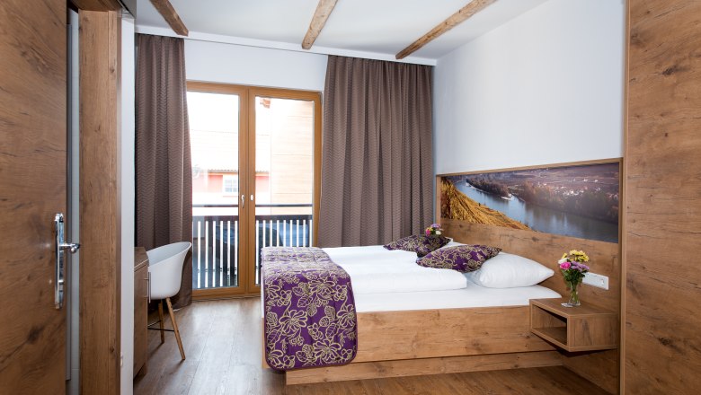 Ein gemütliches Hotelzimmer mit Holzmöbeln, einem Doppelbett, Balkon und dekorativen Kissen.