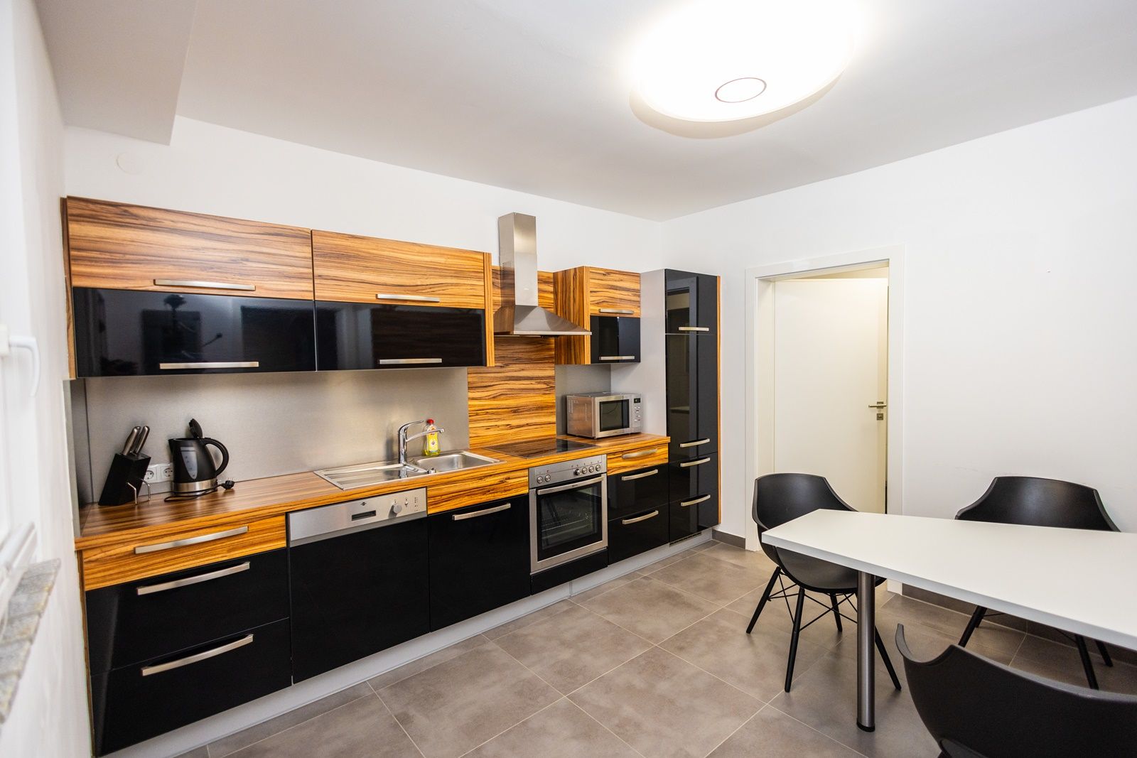 Moderne Küche mit Holz- und schwarzen Hochglanzfronten, Esstisch und Stühlen.