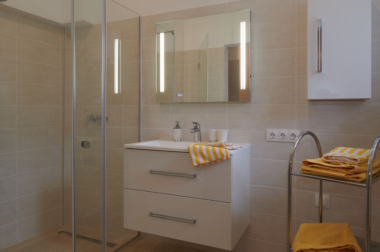 Modernes Badezimmer mit Dusche, Waschbecken und gelben Handtüchern.