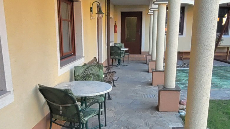 Ein Arkadenhof mit Steinboden, gelber Wand und S&auml;ulen. Tische und St&uuml;hle stehen entlang der Wand.