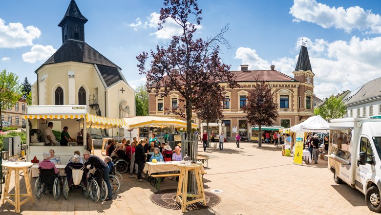 Marktplatz in Gloggnitz mit Kirche, Verkaufsständen und Menschen.