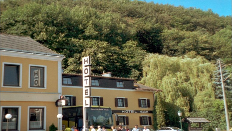 Haus, © Hotel-Gasthof Friedl Ein gelbes Hotelgebäude mit einem großen Hotelschild und Menschen davor, umgeben von Bäumen.