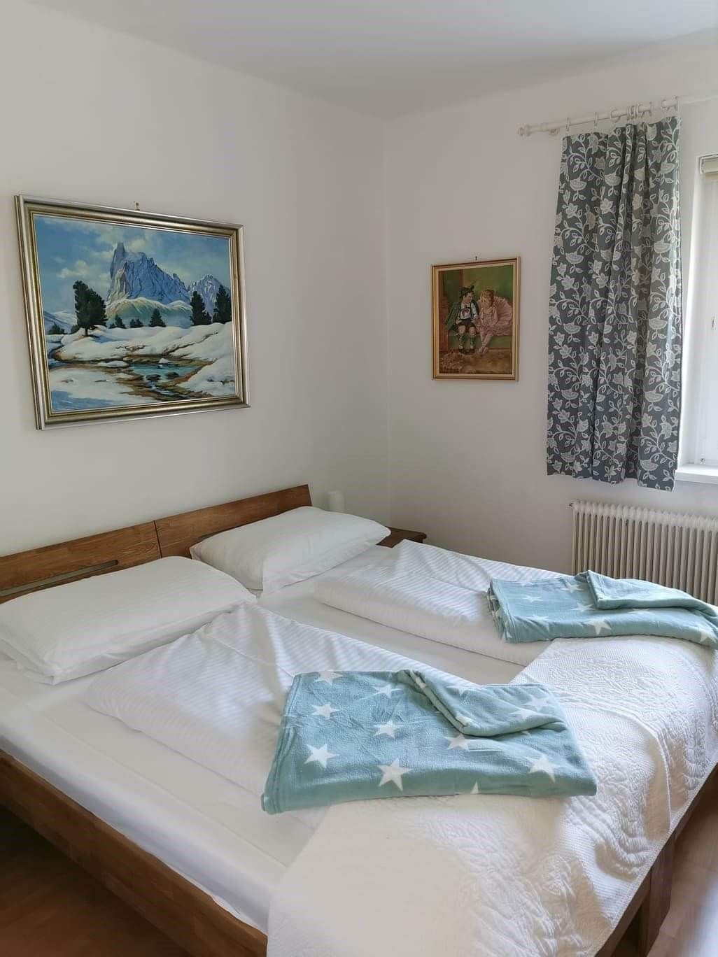 Schlafzimmer mit Doppelbett, zwei Bildern an der Wand und einem Fenster mit Vorhang.