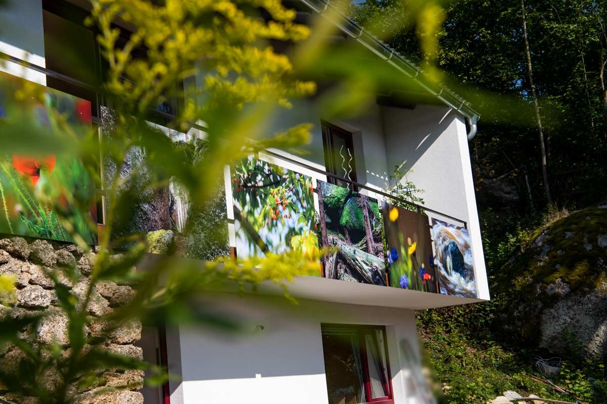 Ein Haus mit einem Balkon, dekoriert mit bunten Naturbildern, umgeben von grüner Vegetation.