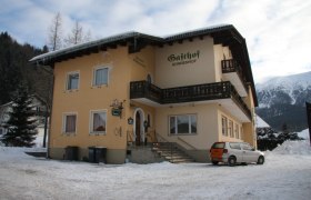 Ein gelbes Geb&auml;ude mit der Aufschrift 'Gasthof Sonnenhof' im Schnee, umgeben von Bergen.