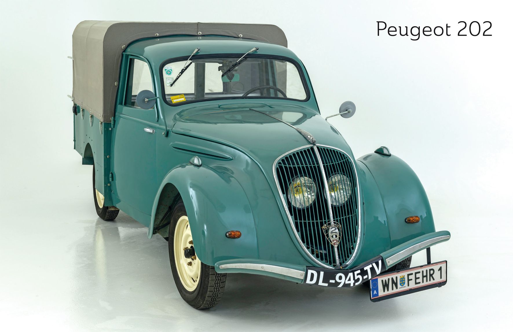 Ein grüner Peugeot 202 mit Plane, frontal fotografiert, auf weißem Hintergrund.