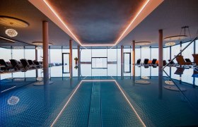 Innenansicht eines Infinitypools mit Liegestühlen und großen Fenstern.