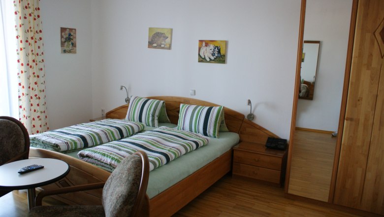 Privatzimmer Würger, © Privatzimmer Würger Ein gemütliches Schlafzimmer mit einem Doppelbett, gestreifter Bettwäsche, zwei Stühlen und einem kleinen Tisch. An der Wand hängen Bilder.