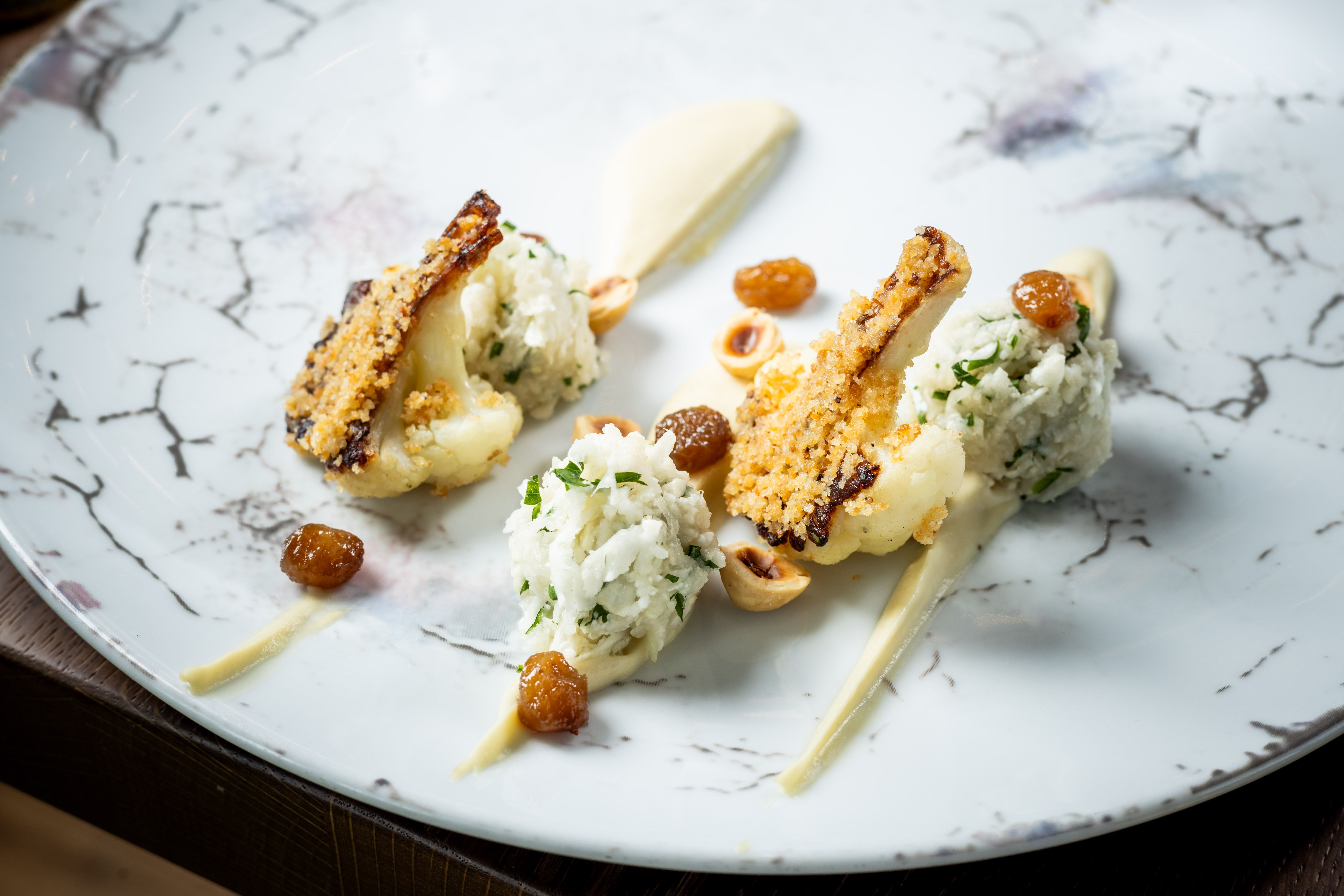 Gourmetgericht mit gebratenem Karfiol, Nüssen und Rosinen auf einem eleganten Teller.