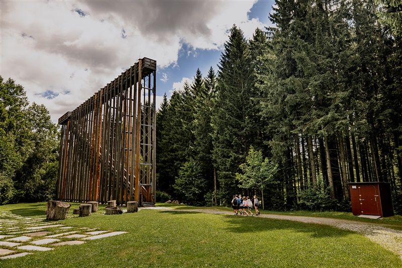 Holzkonstruktion im Wald mit Menschen auf einer Wiese.