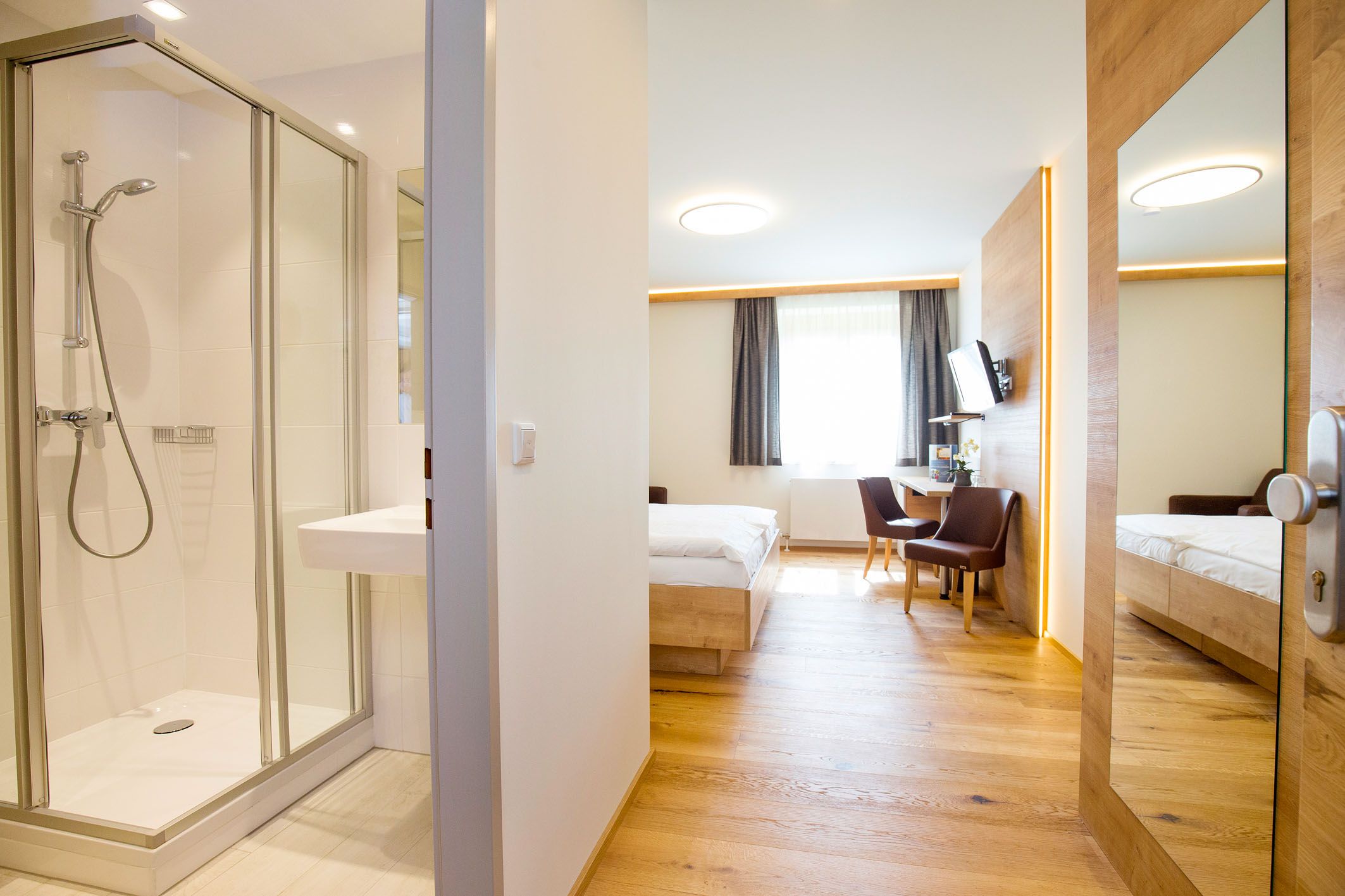 Modernes Hotelzimmer mit Bad, Bett, Schreibtisch und Stühlen.