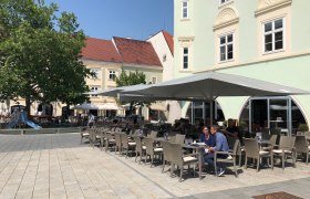 Ein Schanigarten vor dem Eterno mit Sonnenschirmen und Sitzplätzen auf einem gepflasterten Platz.