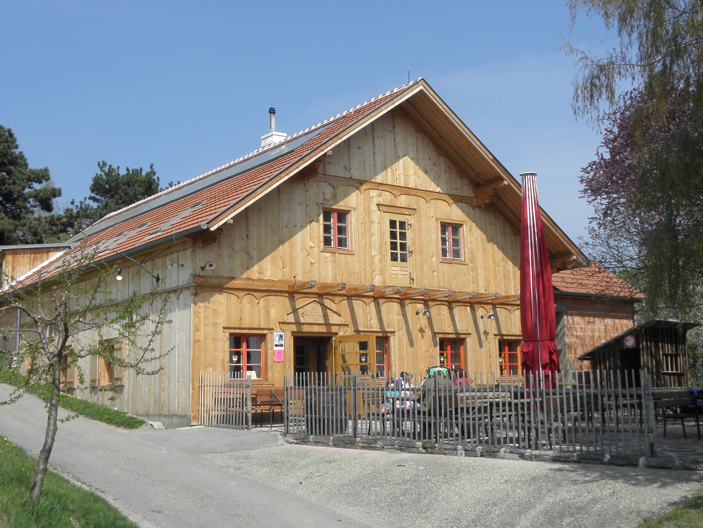 Holzgebäude mit rotem Dach und Zaun, sonniger Tag.