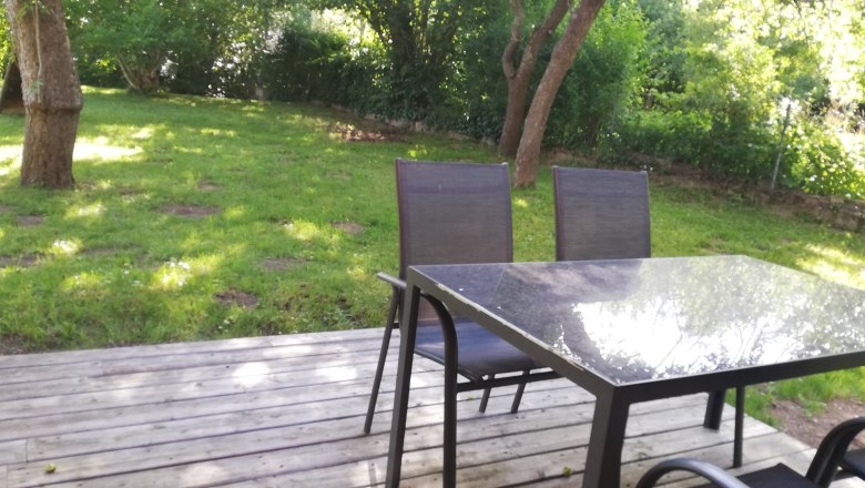 Terrasse mit Tisch und St&uuml;hlen, umgeben von gr&uuml;nem Garten.