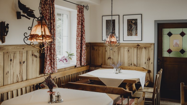 Gem&uuml;tlicher Gastraum mit Holzm&ouml;beln, roten Vorh&auml;ngen und dekorativen Lampen.