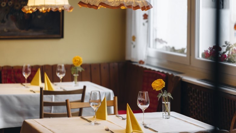 Gem&uuml;tliches Restaurant mit gedeckten Tischen, gelben Servietten und Blumen.