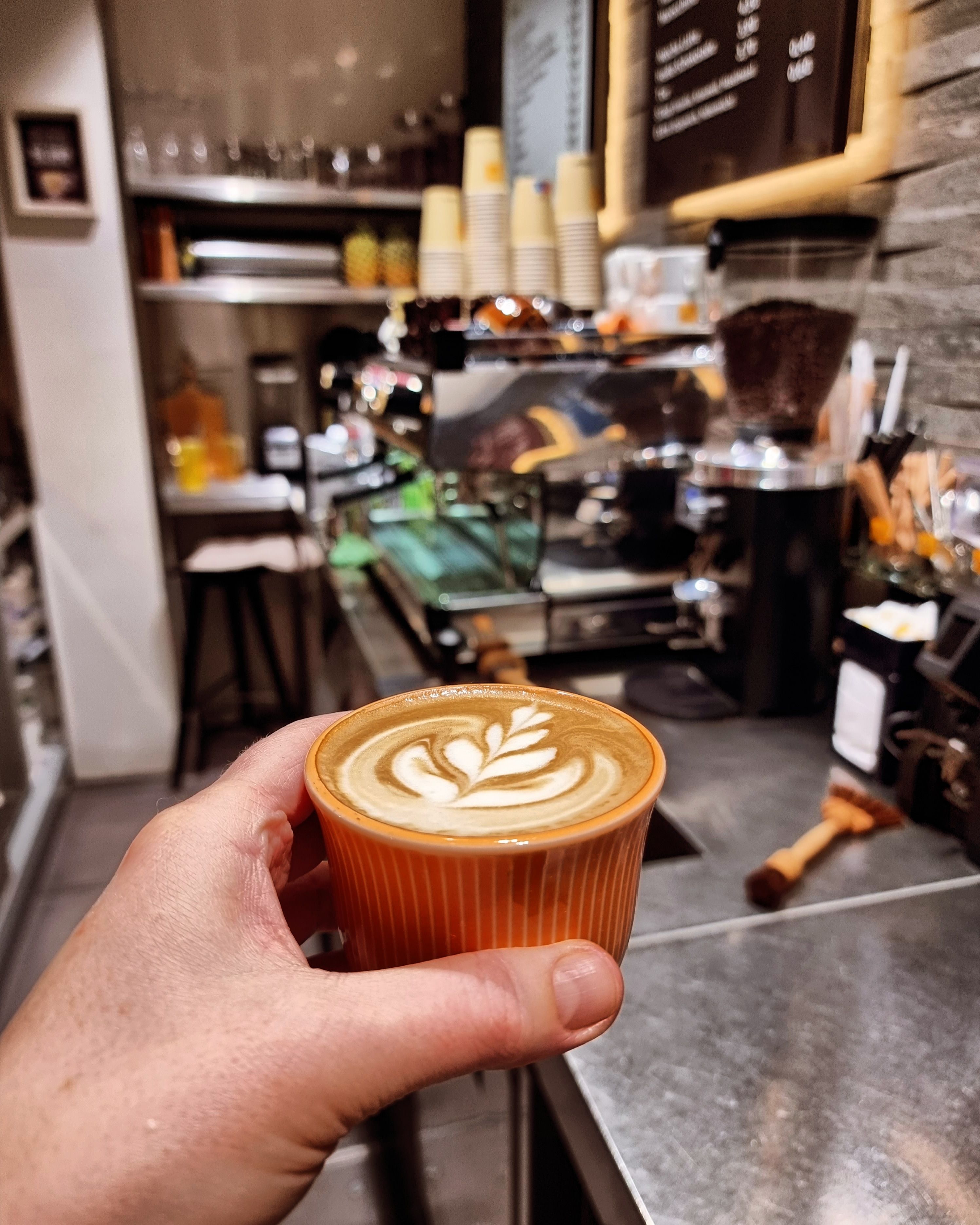 Espresso mit Milchschaum in der Hand gehalten im Hintergrund der Tresen