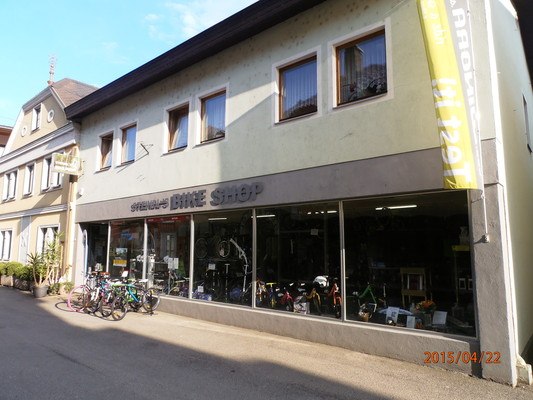 Fahrradgeschäft in einer kleinen Straße mit mehreren Fahrrädern vor dem Schaufenster.