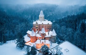 Luftaufnahme von Schloss Ottenstein im Winter, umgeben von schneebedeckten B&auml;umen und beleuchtetem Innenhof.