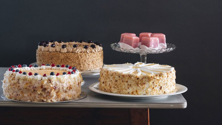 Drei Torten und rosa Gebäck auf einem Tisch.