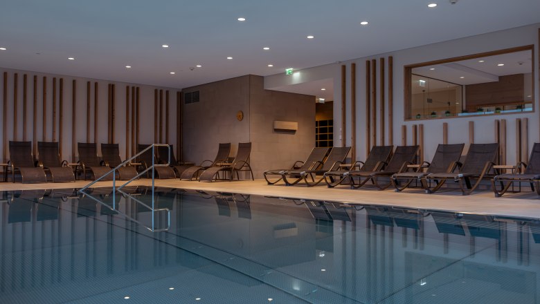 Innenansicht eines Hotelpools mit Liegest&uuml;hlen und moderner Beleuchtung.