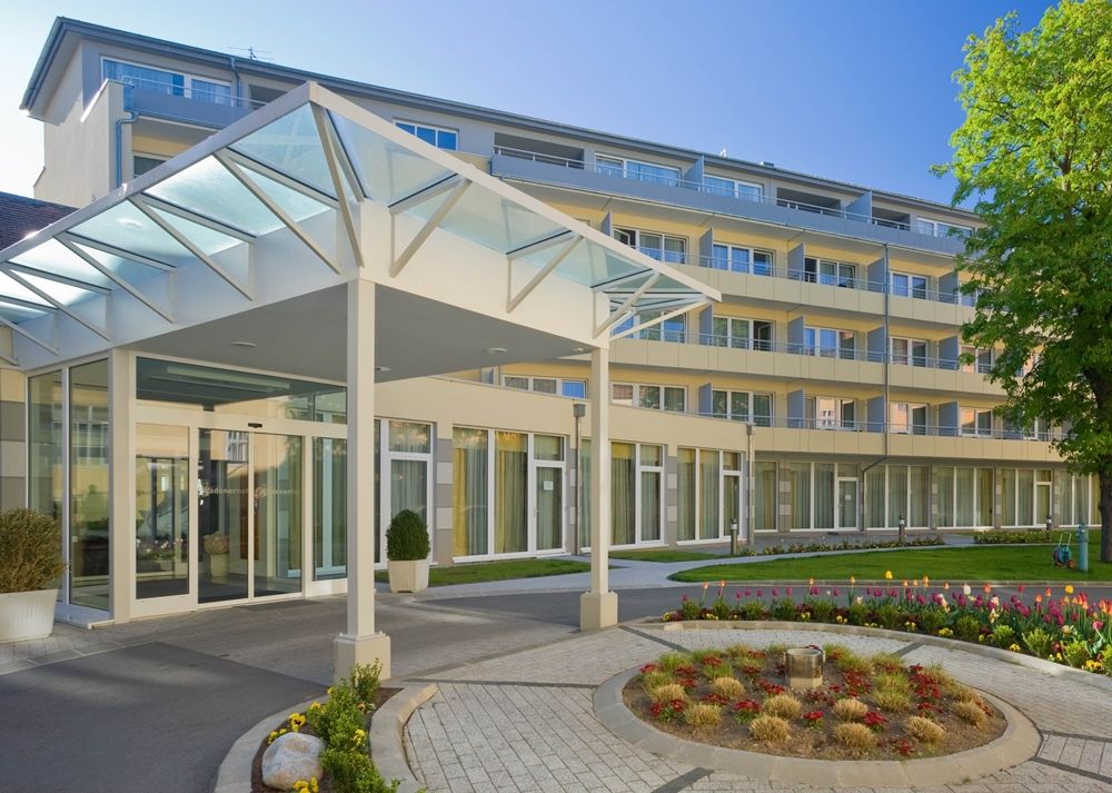 Moderner Gebäudeeingang mit Glasdach und Garten.