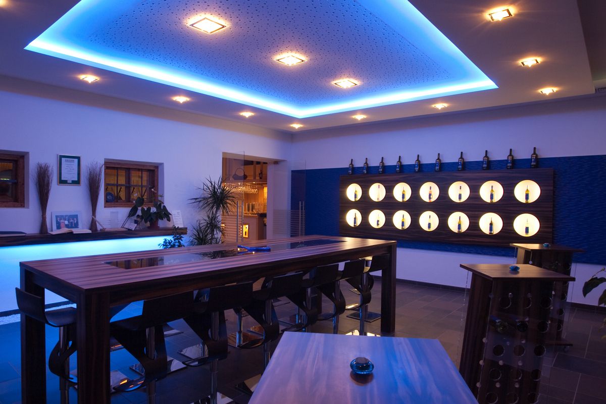 Moderner Verkostungsraum mit blauer Beleuchtung, Holztischen und Weinflaschen an der Wand.