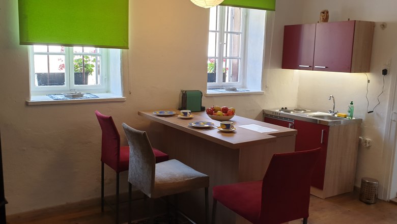 Küche, © Christian Naschitz Küche mit Esstisch, Stühlen und Fenster mit grünem Rollo.