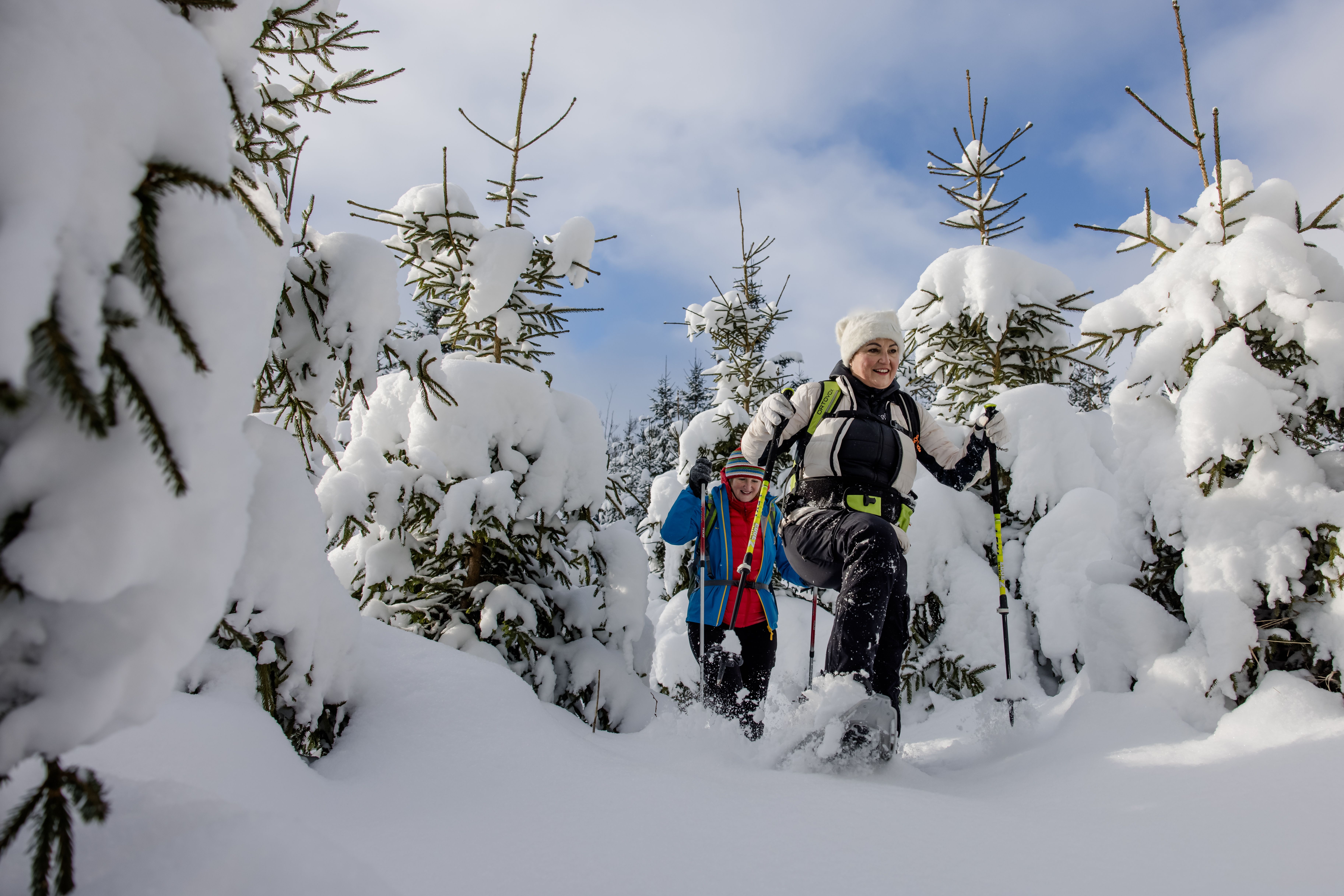 Zwei Personen beim Schneeschuhwandern auf einem verschneiten Feld unter klarem Himmel.