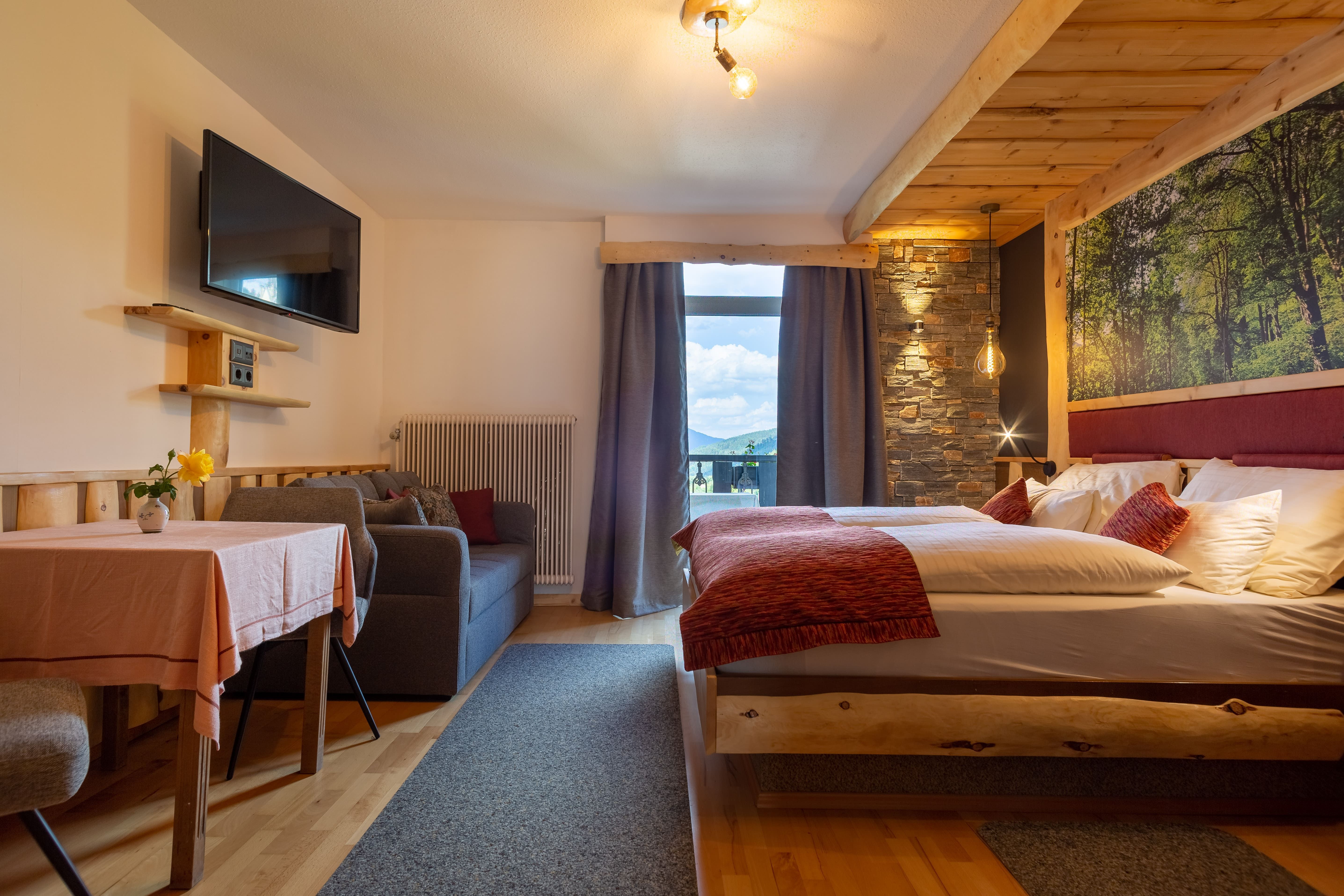 Gemütliches Hotelzimmer mit Doppelbett, Sofa, Tisch und großem Fenster mit Bergblick.