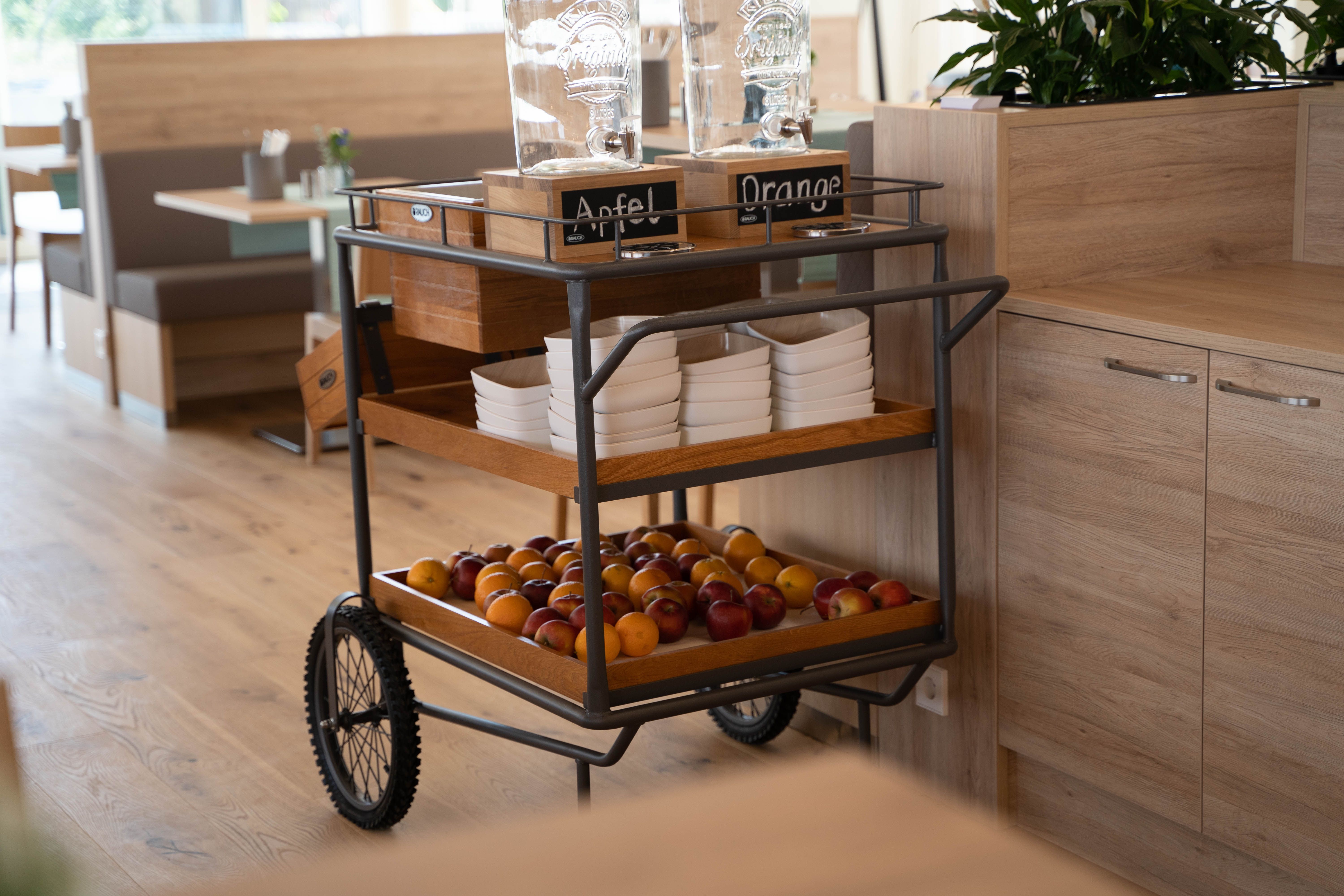 Frühstücksbereich mit einem Servierwagen voller Obst und Getränkespendern.