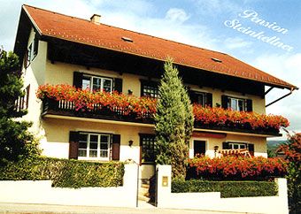 Ein zweistöckiges Haus mit roten Blumen auf den Balkonen, beschriftet mit 'Pension Steinkellner'.