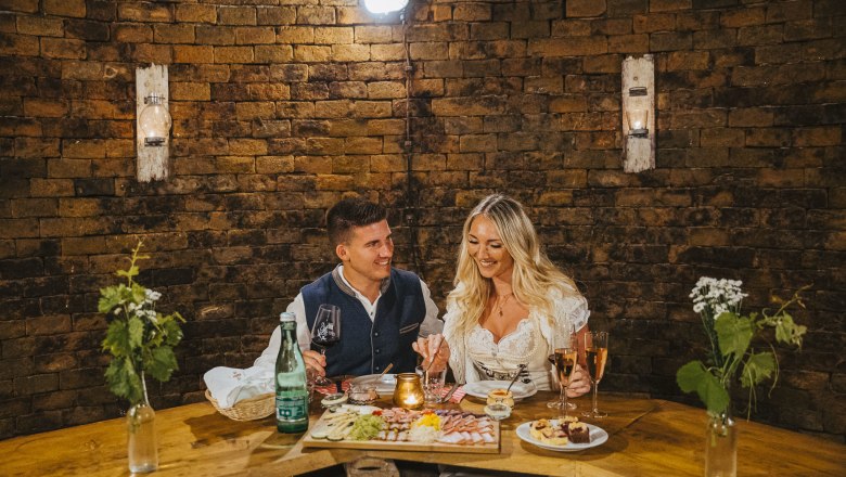 Ein Paar in traditioneller Kleidung genie&szlig;t ein romantisches Abendessen in einem rustikalen Raum mit Backsteinw&auml;nden.