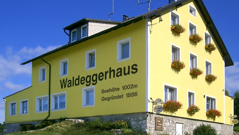 Gelbes Geb&auml;ude mit der Aufschrift 'Waldeggerhaus', umgeben von Blumen.