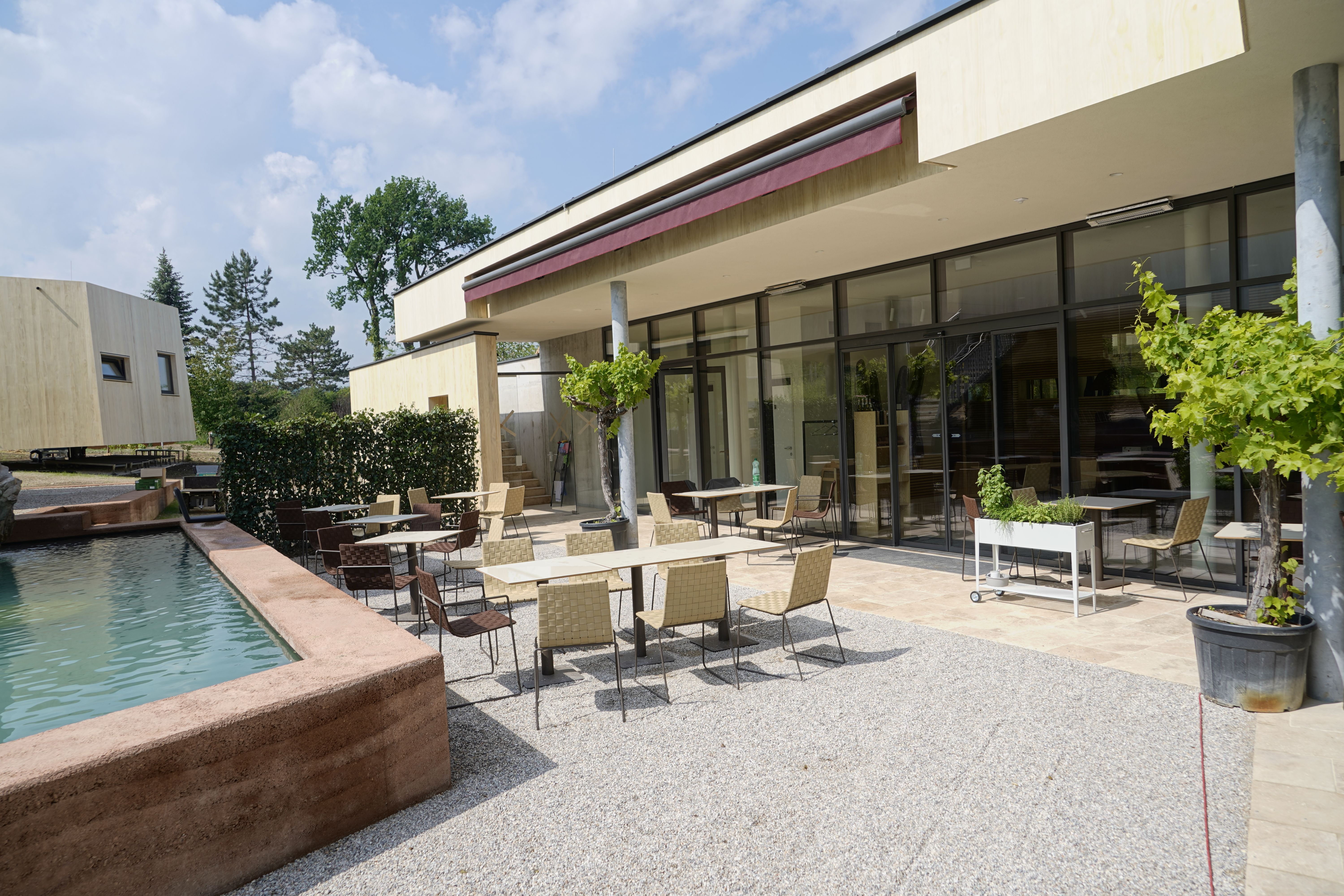 Außenbereich eines modernen Frühstückslokals mit Tischen und Stühlen auf einer Terrasse neben einem Wasserbecken.