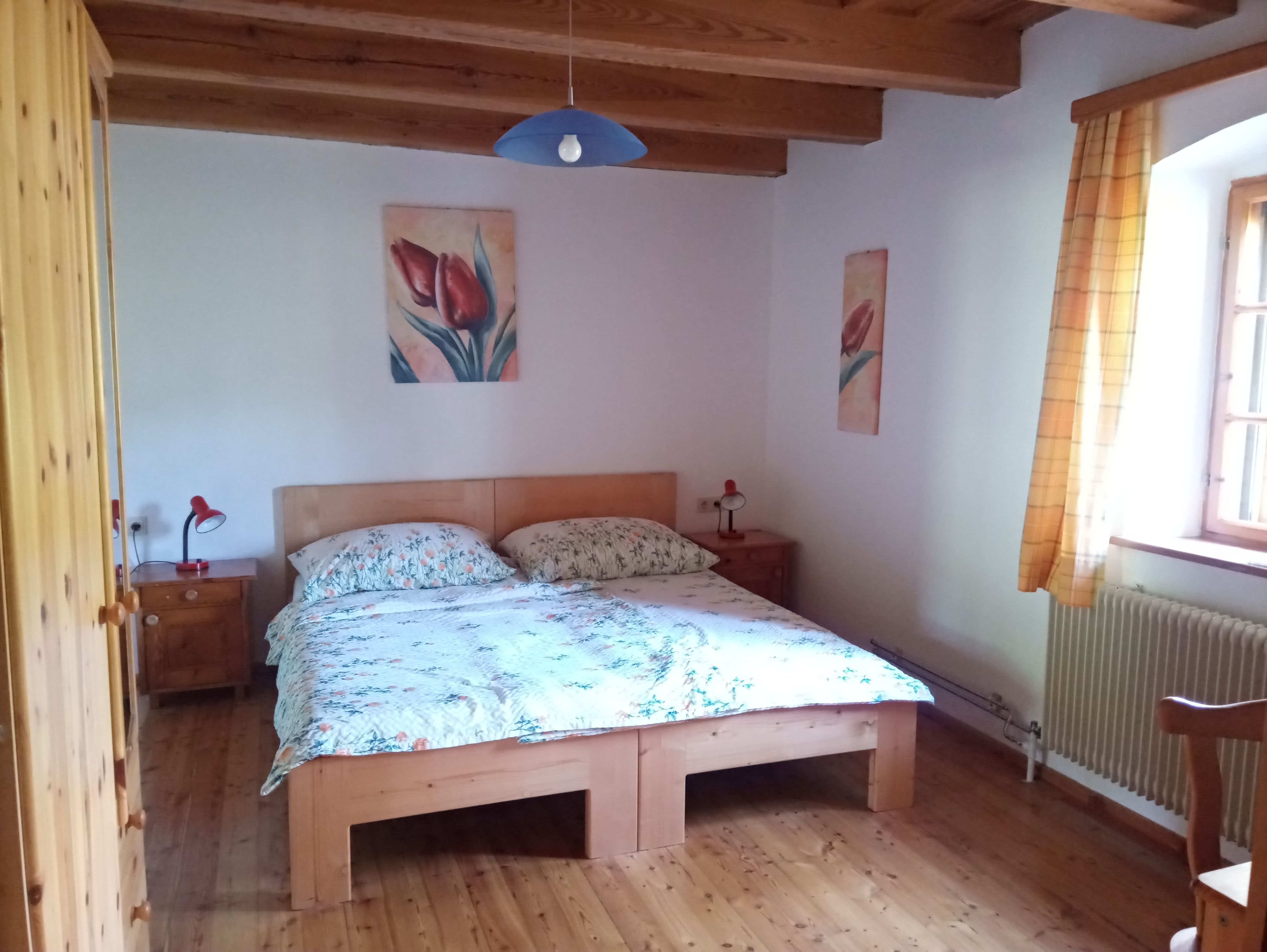 Gemütliches Schlafzimmer mit Holzbett, Nachttischen und Blumenbildern an der Wand.