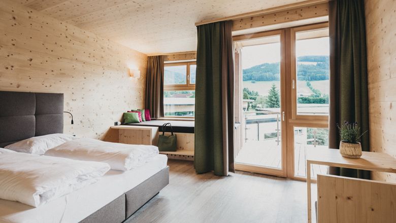 Modernes Hotelzimmer mit Holzwänden, großem Bett und Balkon mit Bergblick.