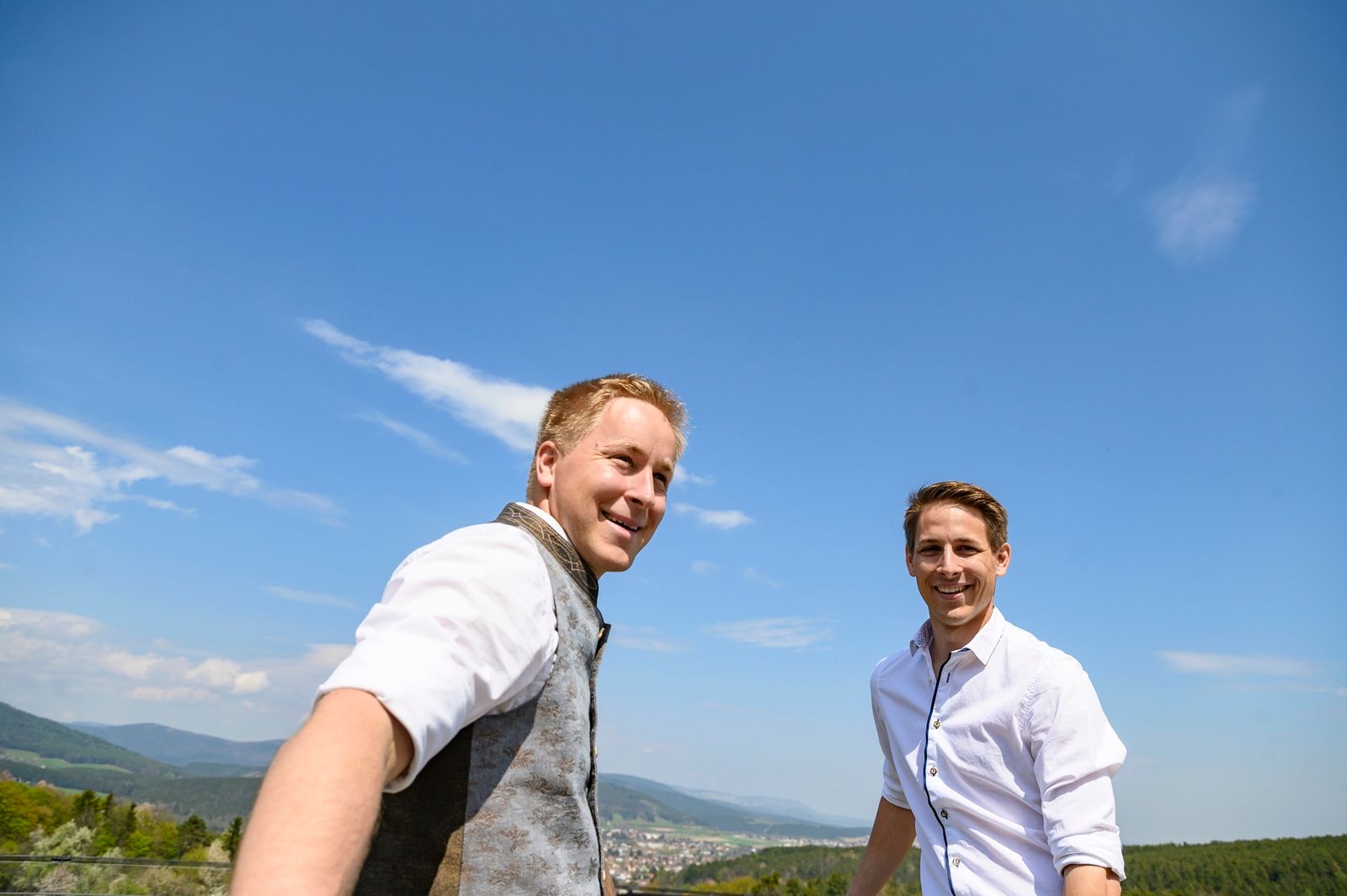 Zwei Männer in traditioneller Kleidung lächeln in die Kamera in einem Obstgarten