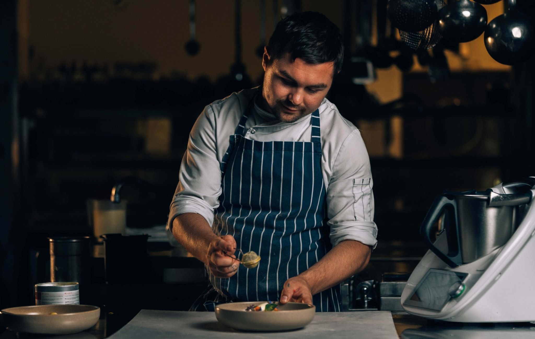 Ein Koch in gestreifter Schürze richtet ein Gericht in einer Küche an.