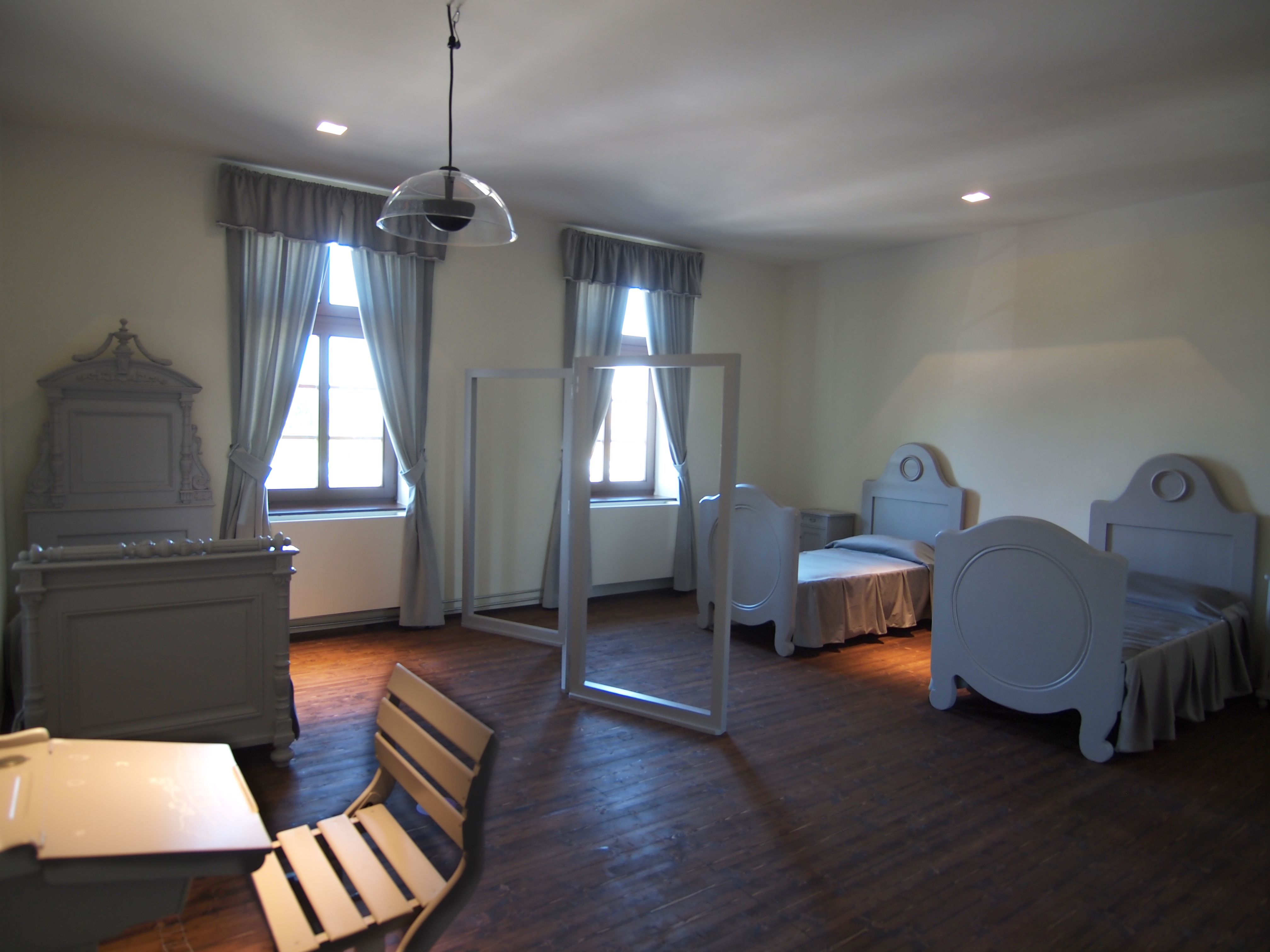 Ein schlicht eingerichtetes Schlafzimmer mit zwei Betten, einem Tisch und Stühlen, alles in grauen Tönen gehalten.