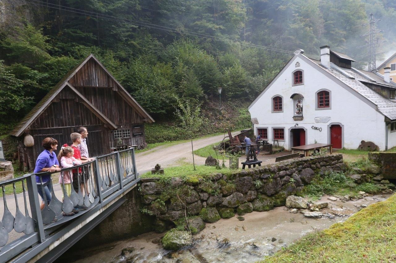 Eine Familie steht auf einer Brücke vor einem historischen Gebäude in einer ländlichen Umgebung.