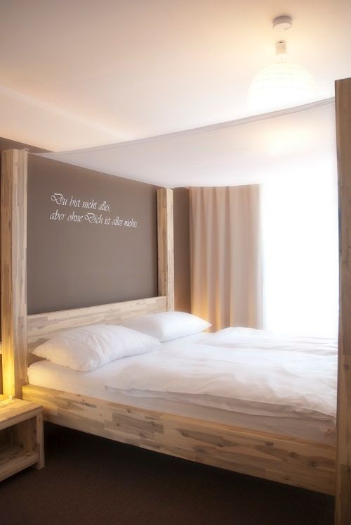 Ein Himmelbett in einem hellen Zimmer mit einem Zitat an der Wand.