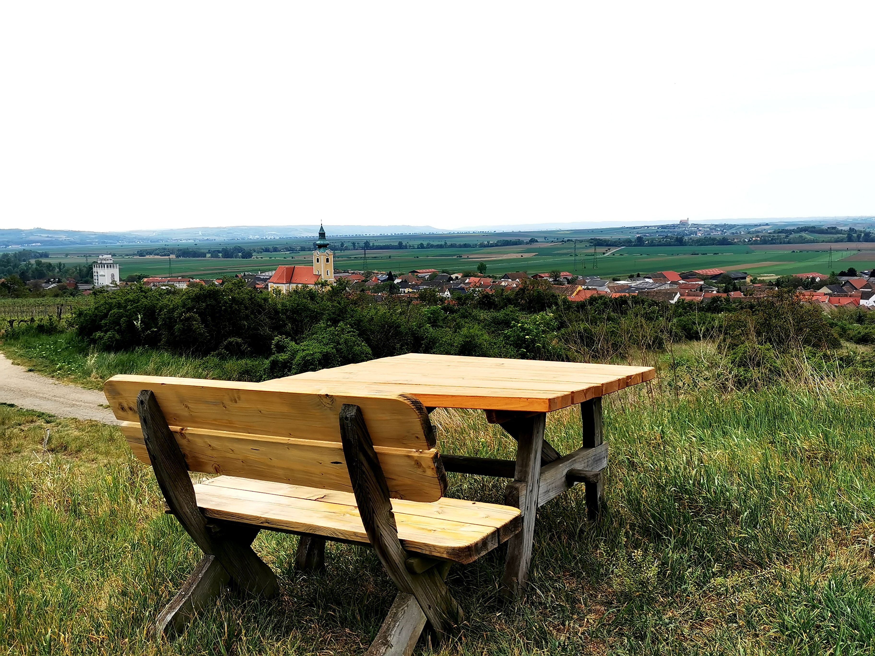Holzbank mit Tisch auf einem Hügel mit Blick auf Röschitz und umliegende Landschaft.