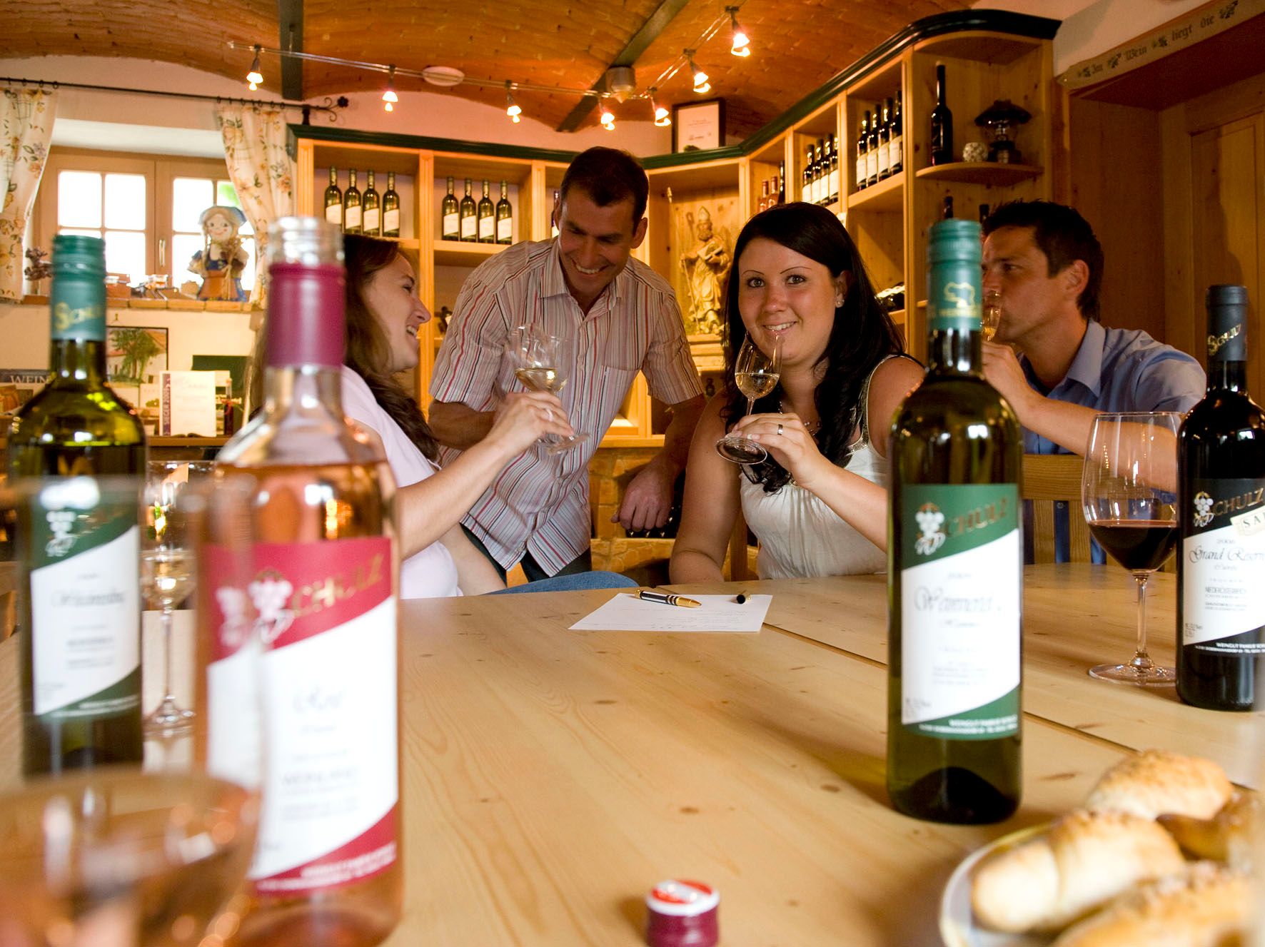 Gruppe von Menschen bei einer Weinprobe in einem gemütlichen Raum mit Weinflaschen auf dem Tisch.