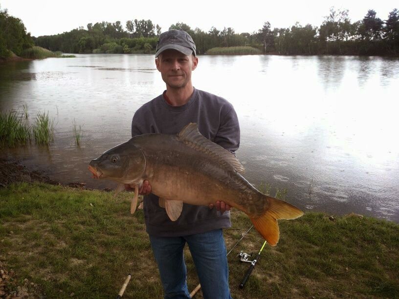 Ein Mann hält einen großen Fisch vor einem See.