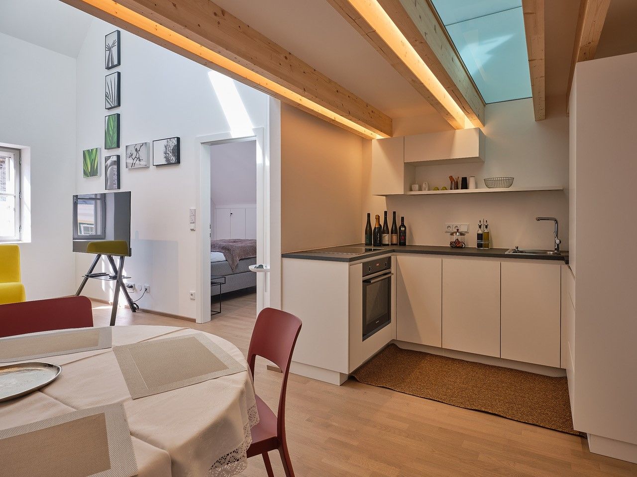 Moderne Küche mit Holzbalken, Esstisch und Blick ins Schlafzimmer.