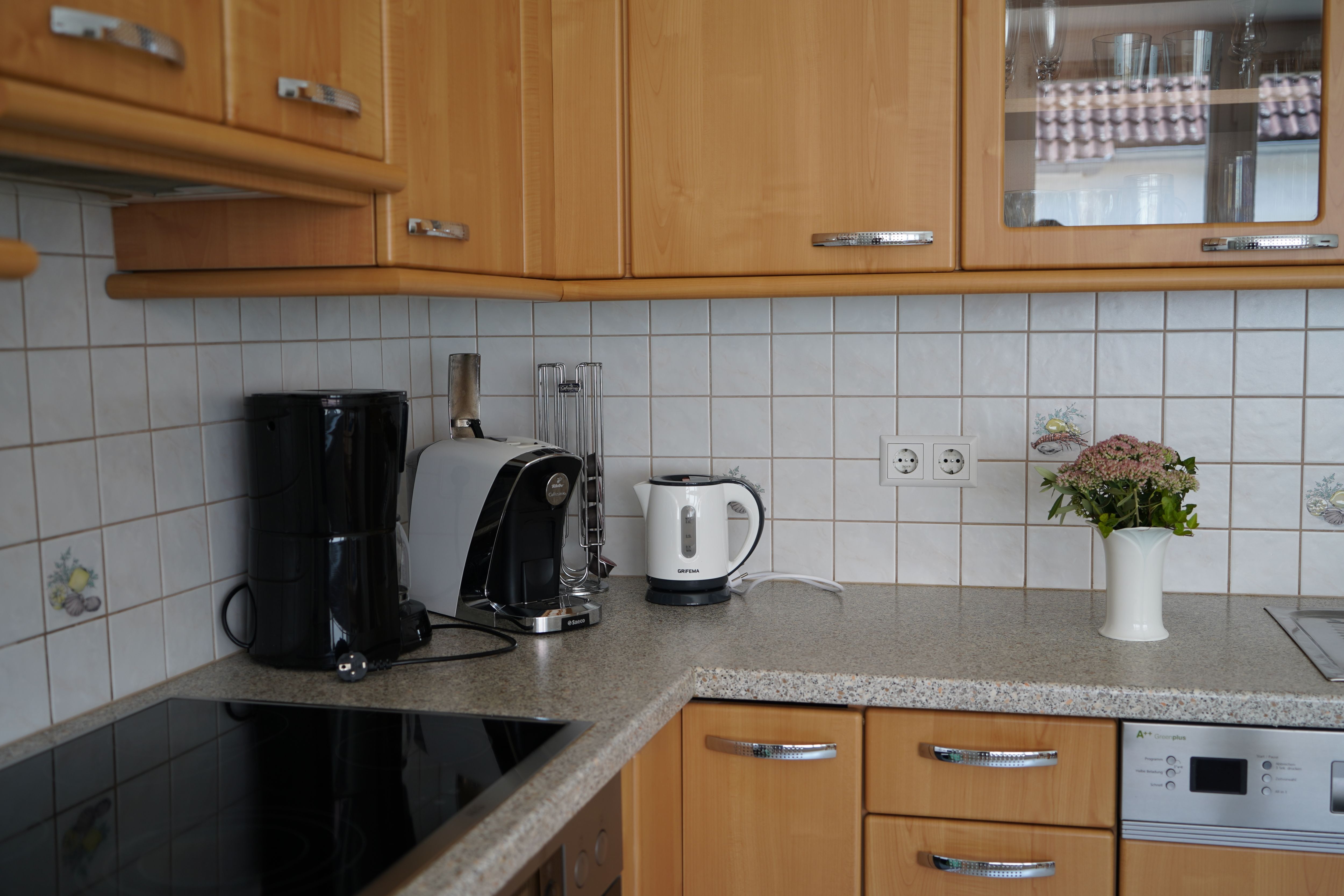 Küchenecke mit Kaffeemaschine, Wasserkocher und Vase auf Arbeitsplatte.