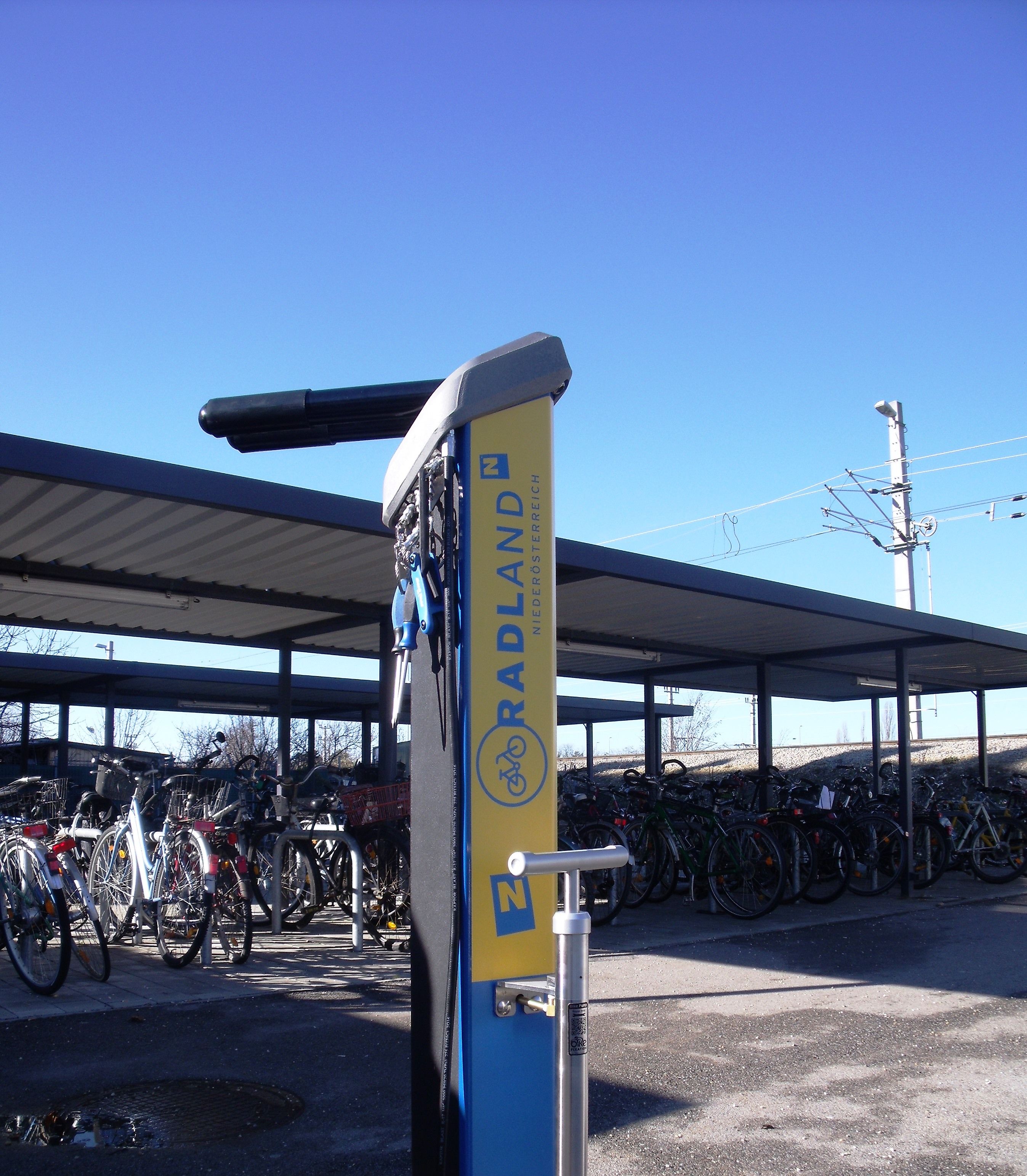 Fahrradstation mit Werkzeugen und Luftpumpe vor einem überdachten Fahrradabstellplatz.